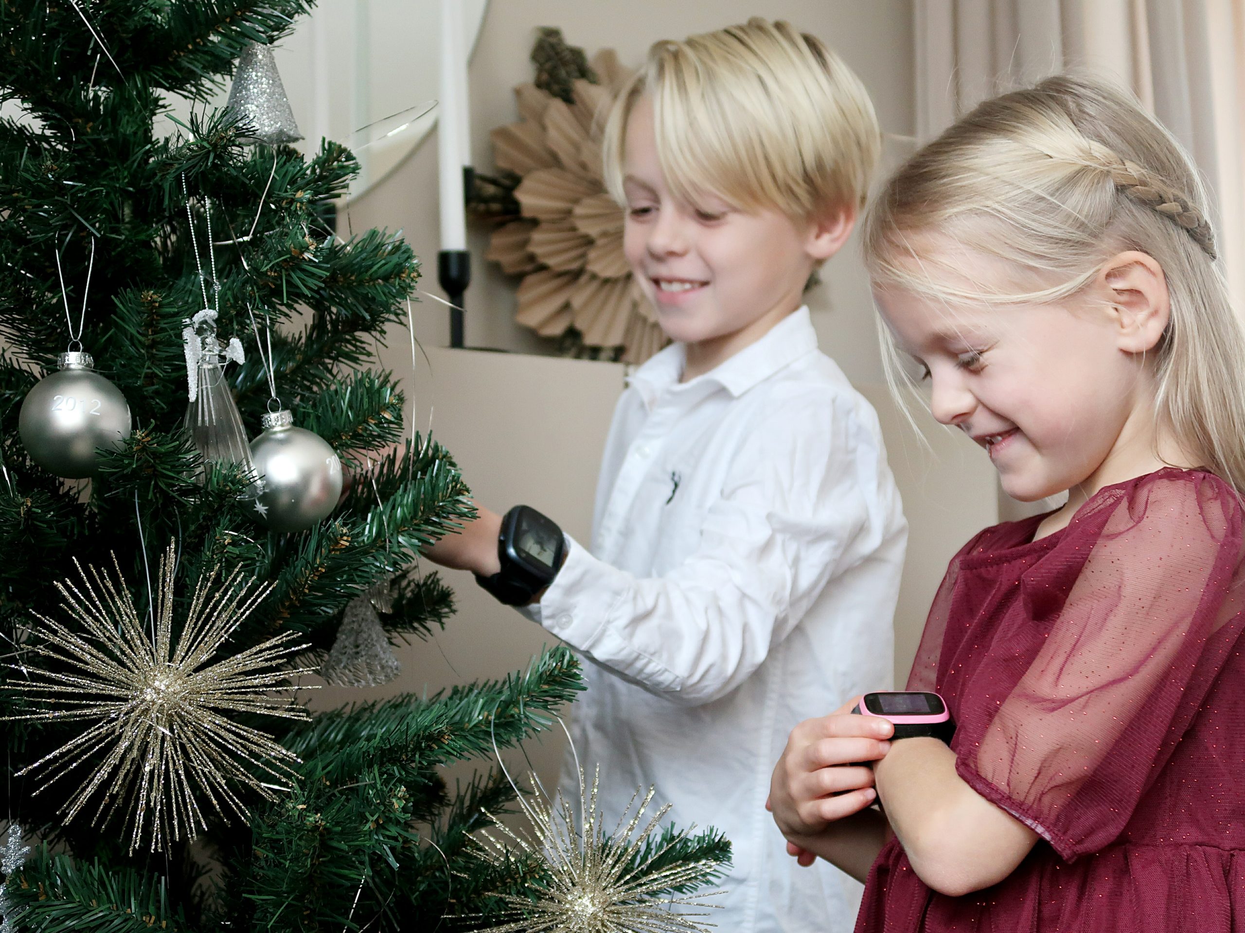 1 flicka står med röd klänning och 1 kille med vit skjorta står vid en julgran, aktivera din Xplora
