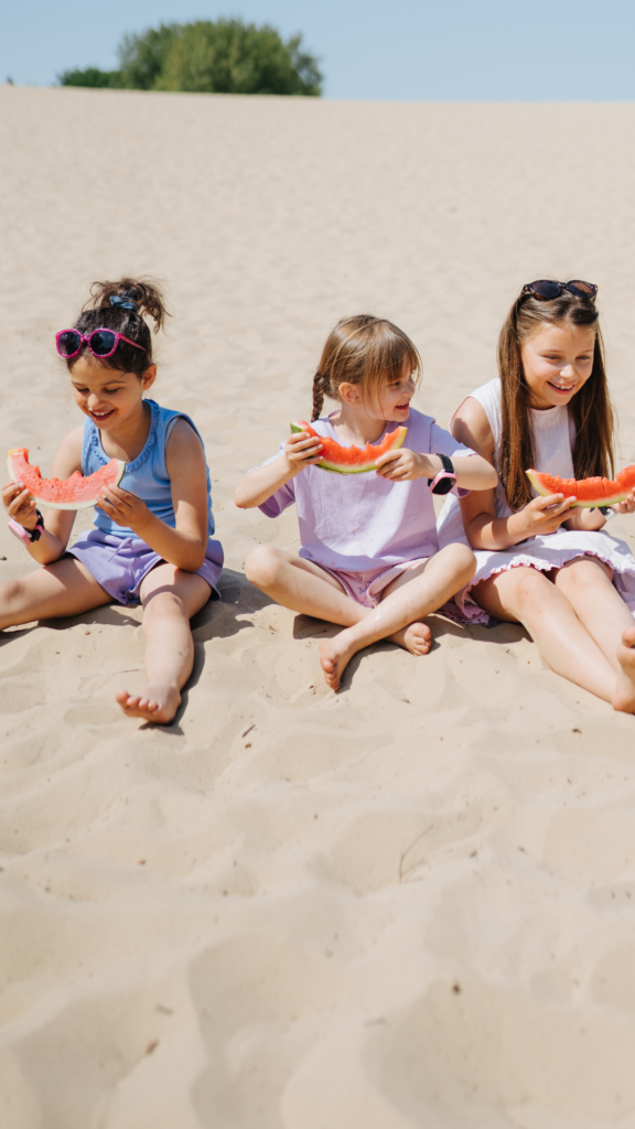 Barn sitter på stranden och äter vattenmelon med Xplora smartklocka för barn på handleden